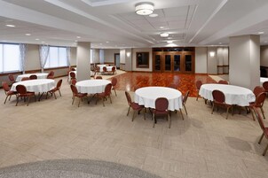 A conference room with round tables and chairs, carpeted flooring, and large windows with curtains.