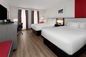 A hotel room with two beds, a desk, a chair, a TV, and a lamp.