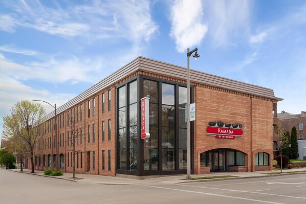 Un edificio de ladrillo con ventanas amplias y un letrero que dice 'RAMADA BY WYNDHAM'.