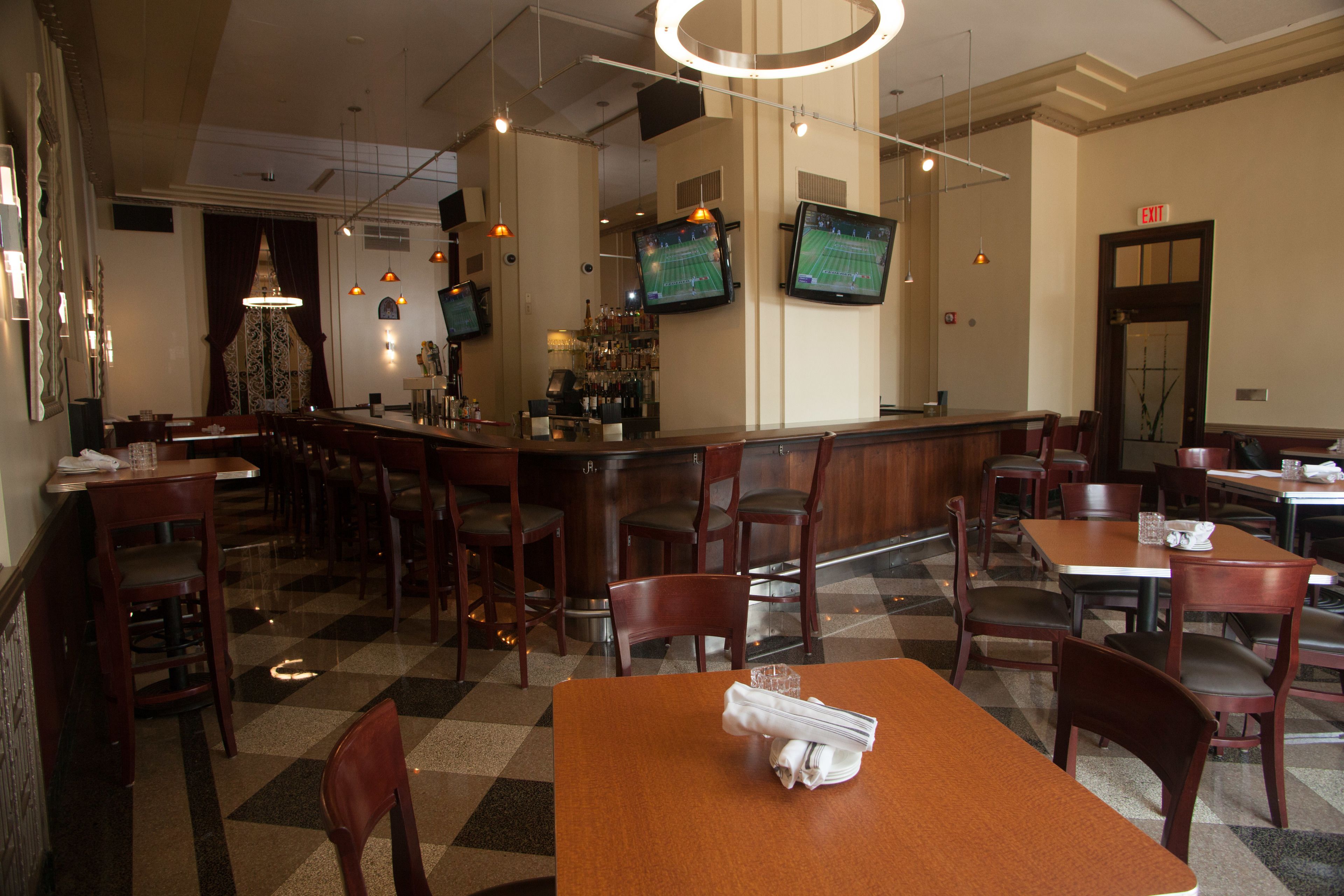 A restaurant with a bar area, multiple tables and chairs, and two screens displaying a tennis game.