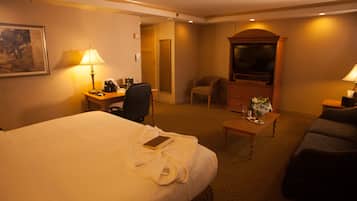 A hotel room with a large bed, a desk with a lamp, a television, a chair, and a sofa.