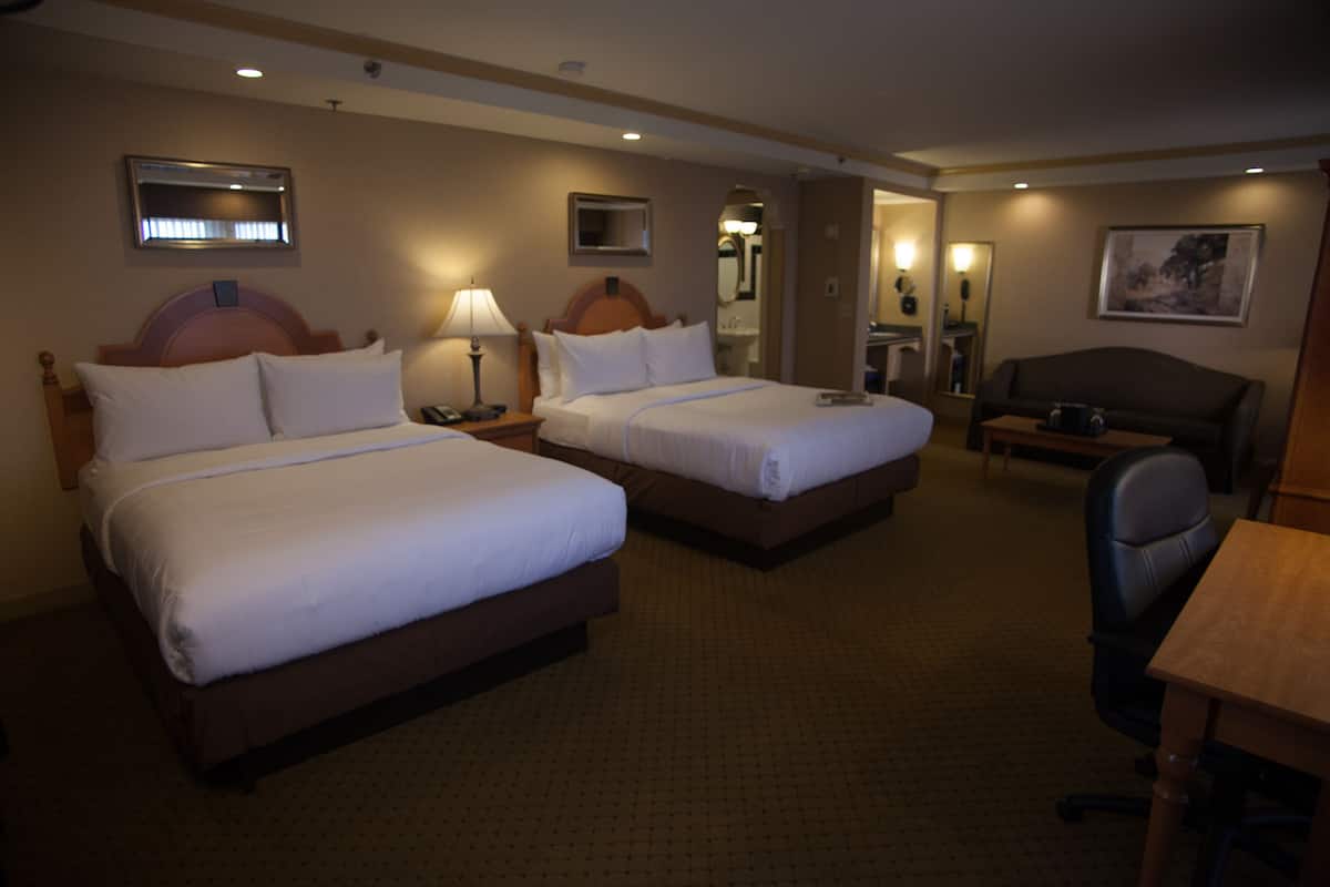 A hotel room with two beds, a desk, a chair, and a mirror.