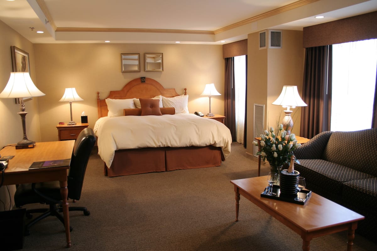 A hotel room with a large bed, a desk with a chair, a sofa, and two lamps.