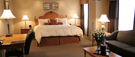 A hotel room with a large bed, a desk with a chair, a sofa, and two lamps.