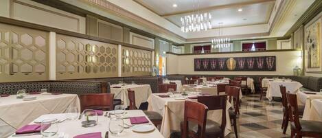 A restaurant with multiple tables set for dining, featuring a checkered floor pattern and a chandelier.