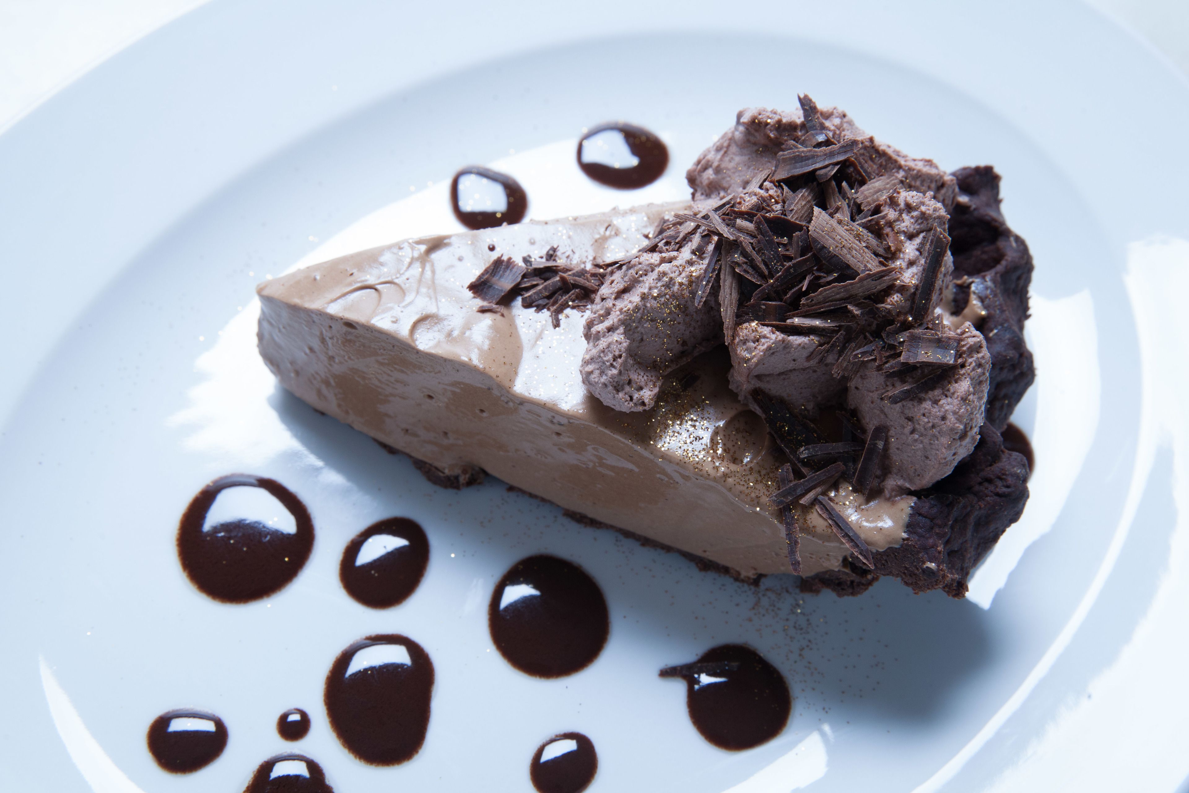 Un postre en un plato blanco con virutas de chocolate y salsa de chocolate.