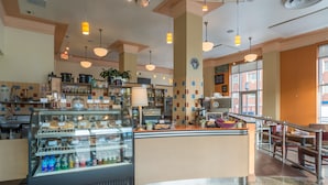 A bakery counter with baked goods and a coffee machine, a seating area with tables and chairs, and a large window with a view of the street. - Ambassador Hotel Milwaukee, Trademark Collection by Wyndham (Milwaukee)