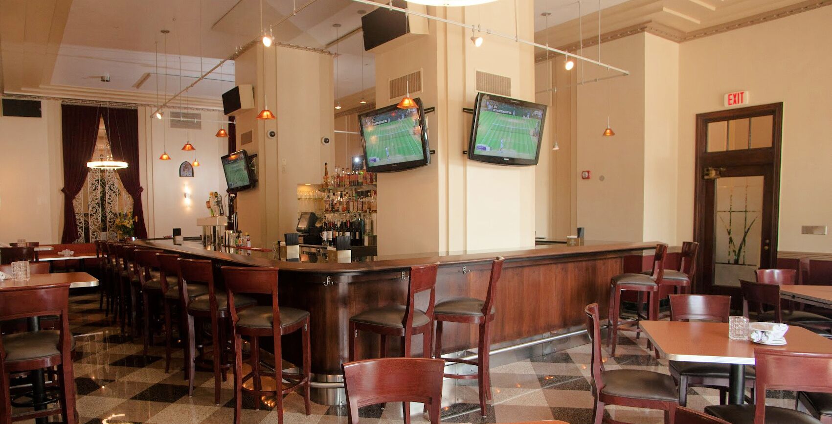 Un área de bar con varias pantallas mostrando deportes, una barra y varias mesas y sillas de madera.