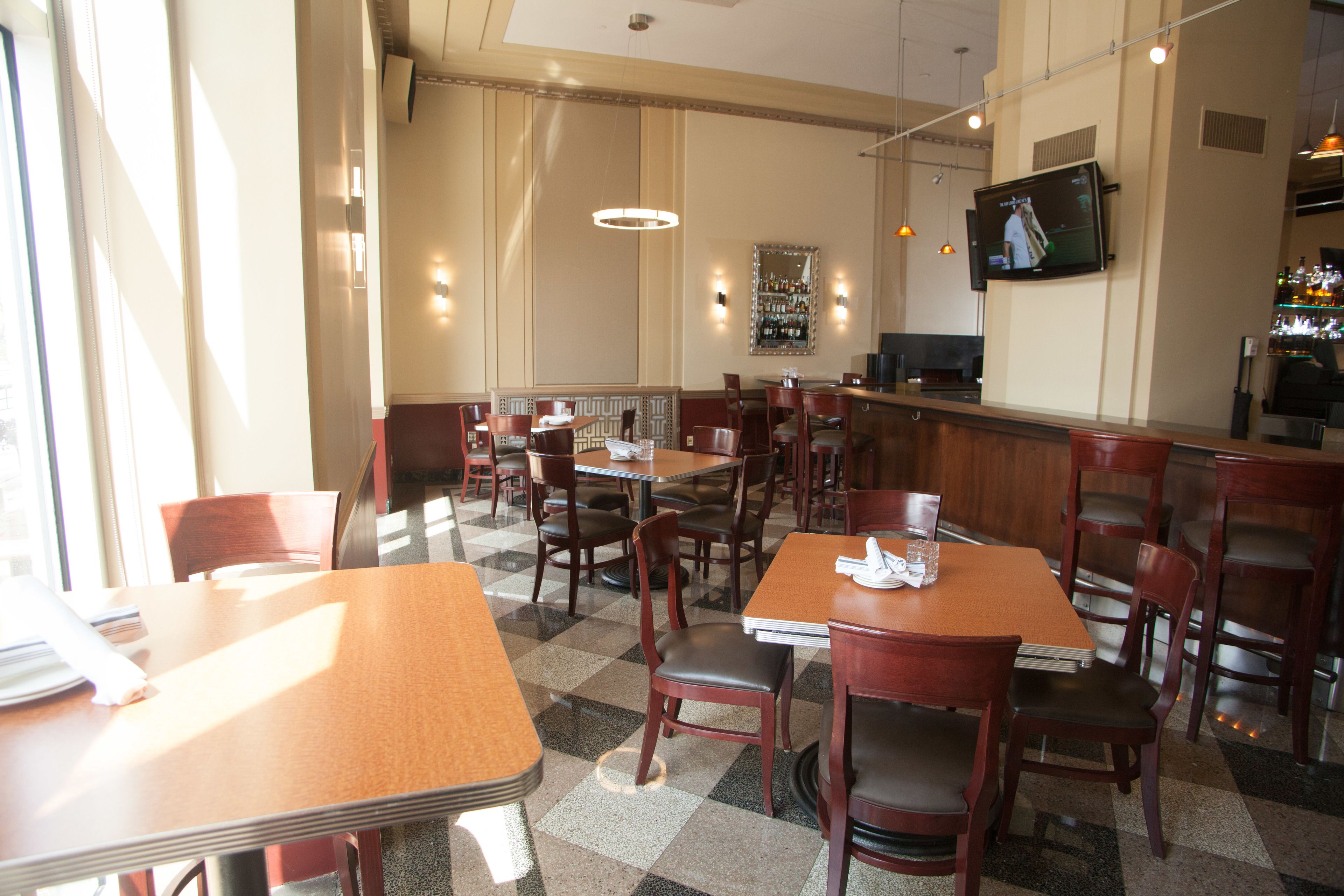 A restaurant with multiple tables and chairs, a bar area, and a television screen on the wall.