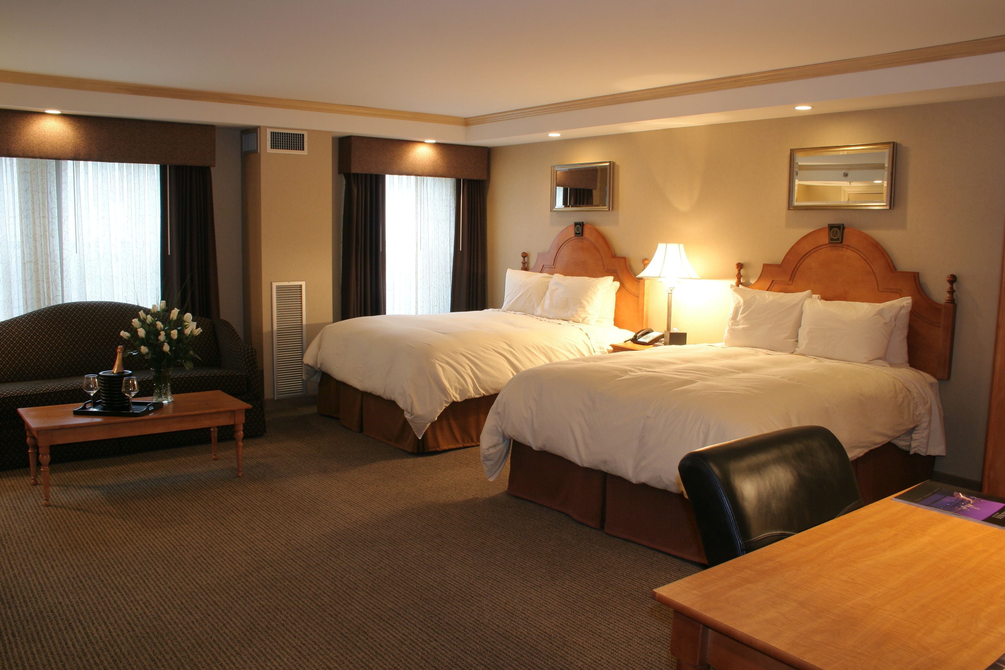 Habitación de hotel con dos camas, un escritorio, una silla, una mesa de centro con un jarrón de flores y una lámpara.