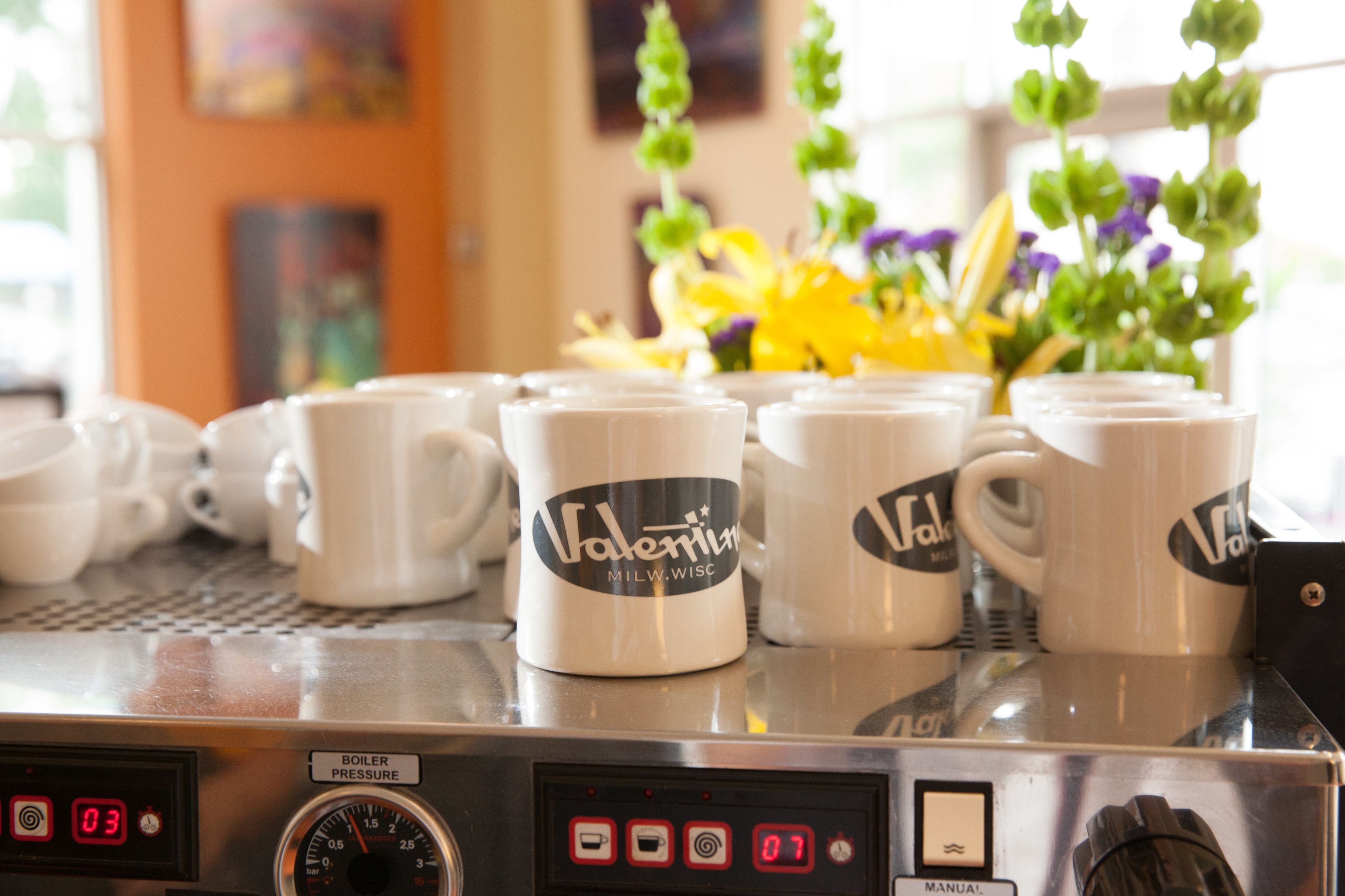 A coffee machine with several coffee cups labeled "Valentina" and a digital display.