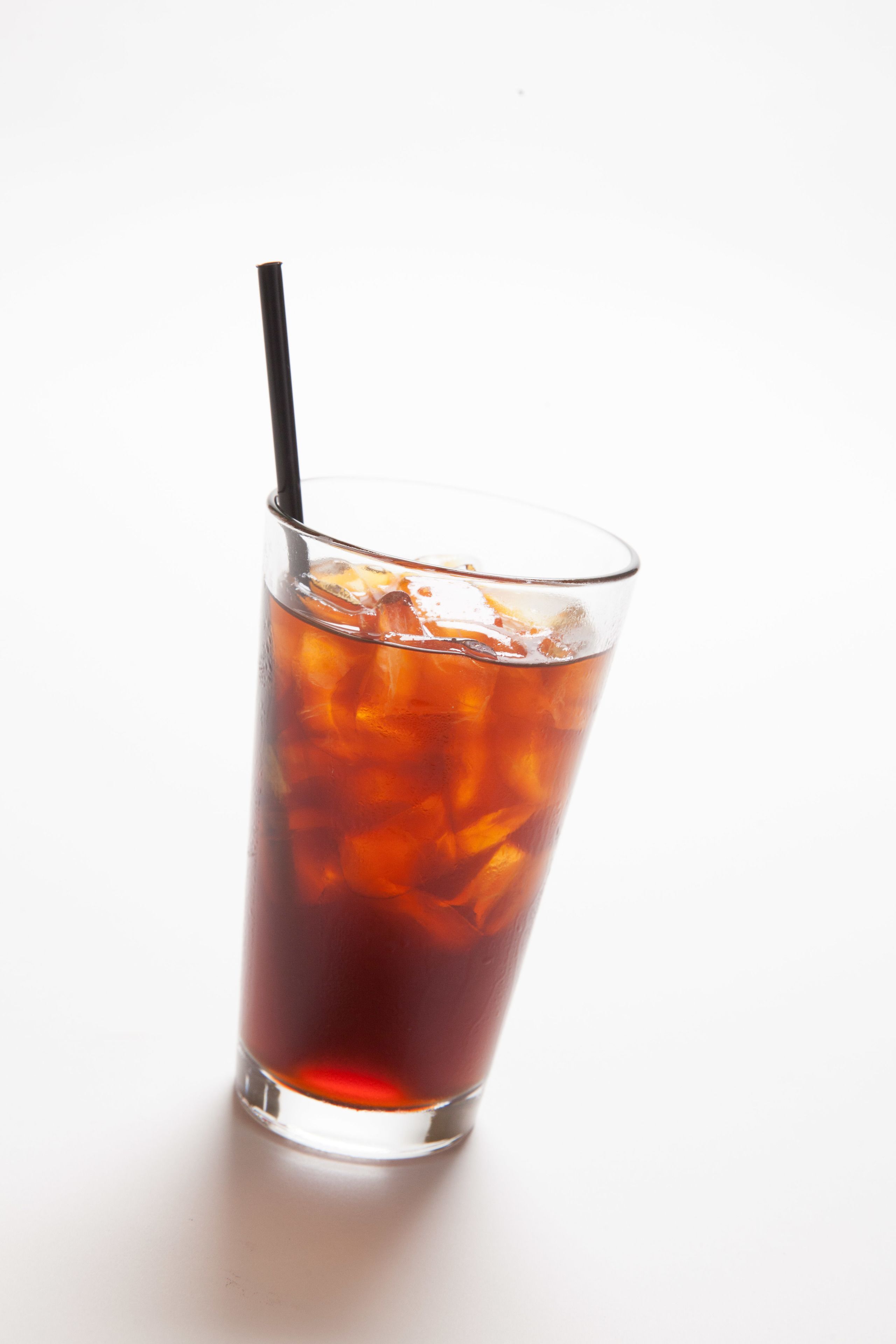 Un vaso alto con pajita, lleno de un líquido oscuro y cubitos de hielo.