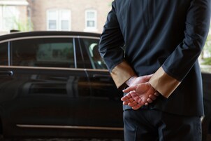 Una persona in un abito scuro in piedi di fronte a un'auto nera.