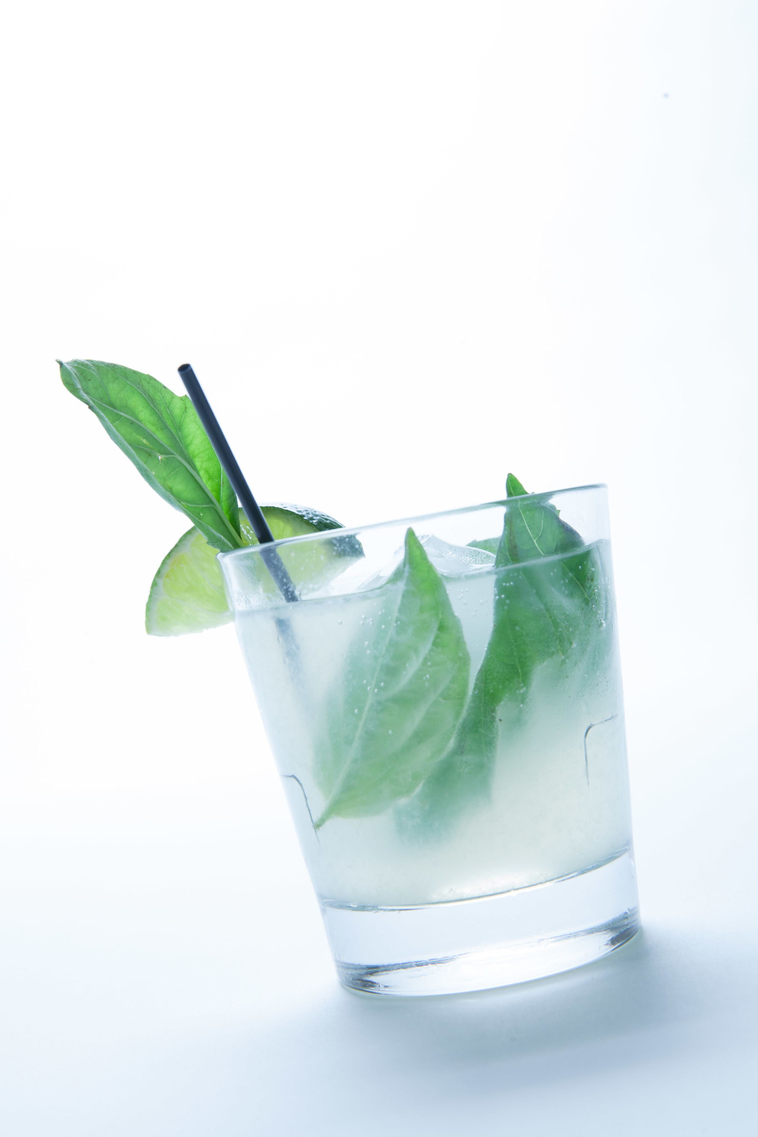 A clear glass with ice cubes and mint leaves, with a black straw.