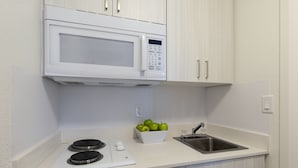 Una cocina con microondas, un lavamanos, una tabla de cortar y un bol con manzanas.