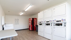 Un área de lavandería con varias lavadoras, una máquina expendedora de Coca-Cola y una mesa blanca.