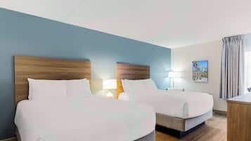 Une chambre d’hôtel avec deux lits, un bureau, une lampe et un tableau au mur.