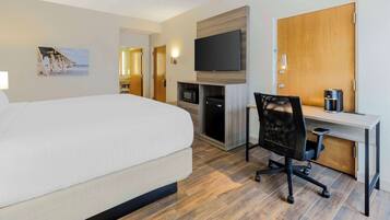 Una habitación de hotel con una cama, un escritorio con una silla, un televisor, un microondas y una cafetera.