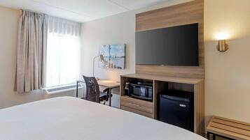 Une chambre d’hôtel avec un grand lit, un bureau avec une chaise, un four à micro-ondes, un réfrigérateur, un téléviseur à écran plat fixé au mur et un tableau accroché au mur.
