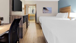 A hotel room with a bed, a desk with a chair, a TV mounted on the wall, and a bathroom visible through an open door.