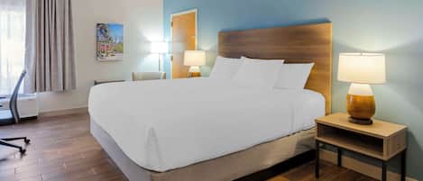 Una cama bien hecha con sábanas blancas, dos lámparas de noche, una mesita de madera y un cuadro en la pared.