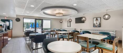 Un restaurante con mesas redondas y cabinas, un área de cocina y vistas al exterior.