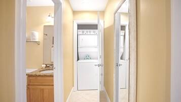 Un couloir étroit, avec une salle de bain sur la gauche, comprenant un lavabo et des toilettes. On peut apercevoir un appareil électroménager blanc dans la salle de bain.