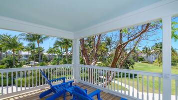 A covered outdoor area with a wooden deck, white railing, and blue chairs.