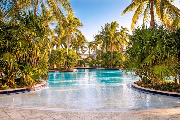 Una piscina rodeada de palmeras y un sendero con baldosas.