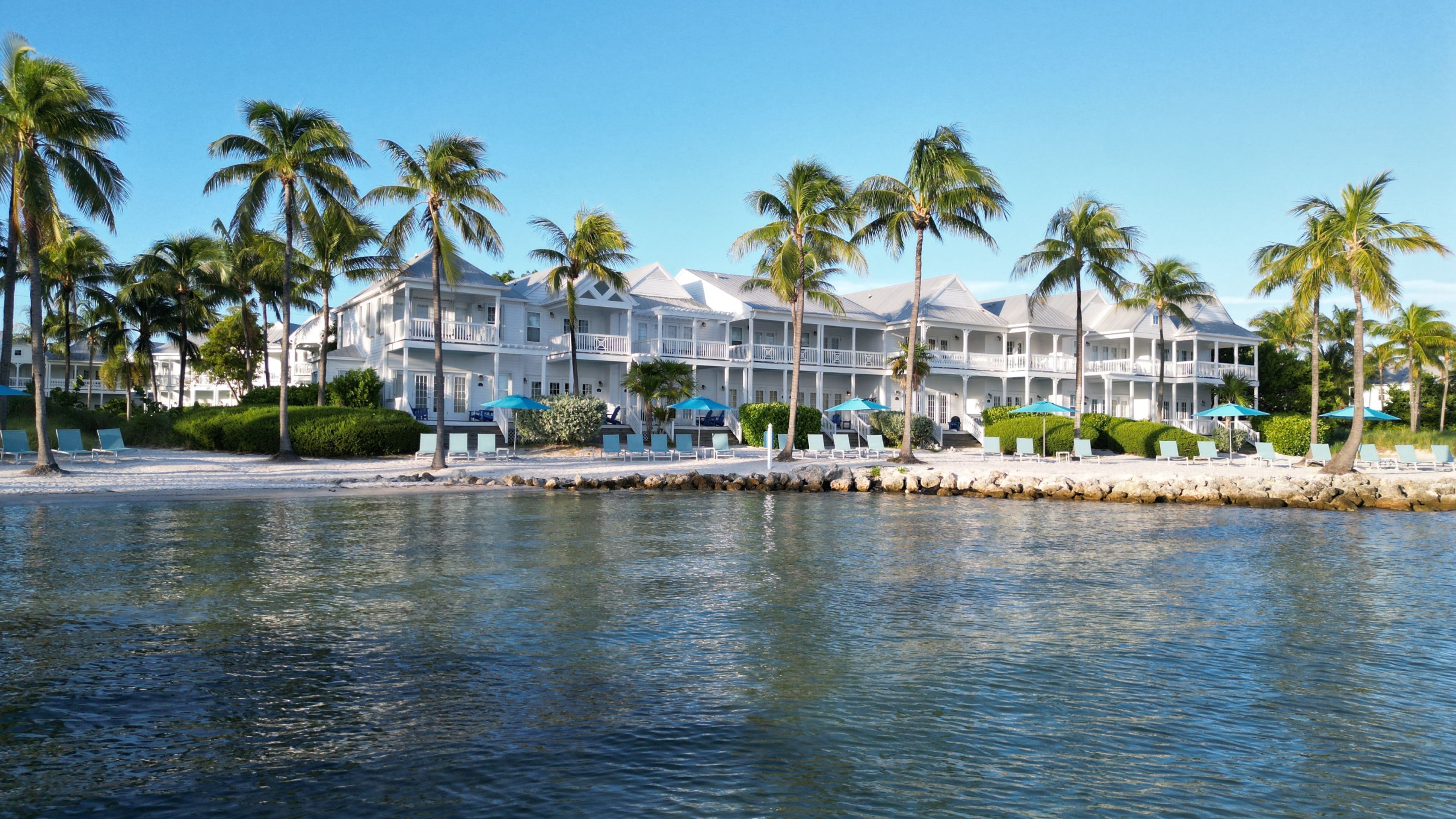 A beachfront hotel with multiple balconies, palm trees, and a pool area.