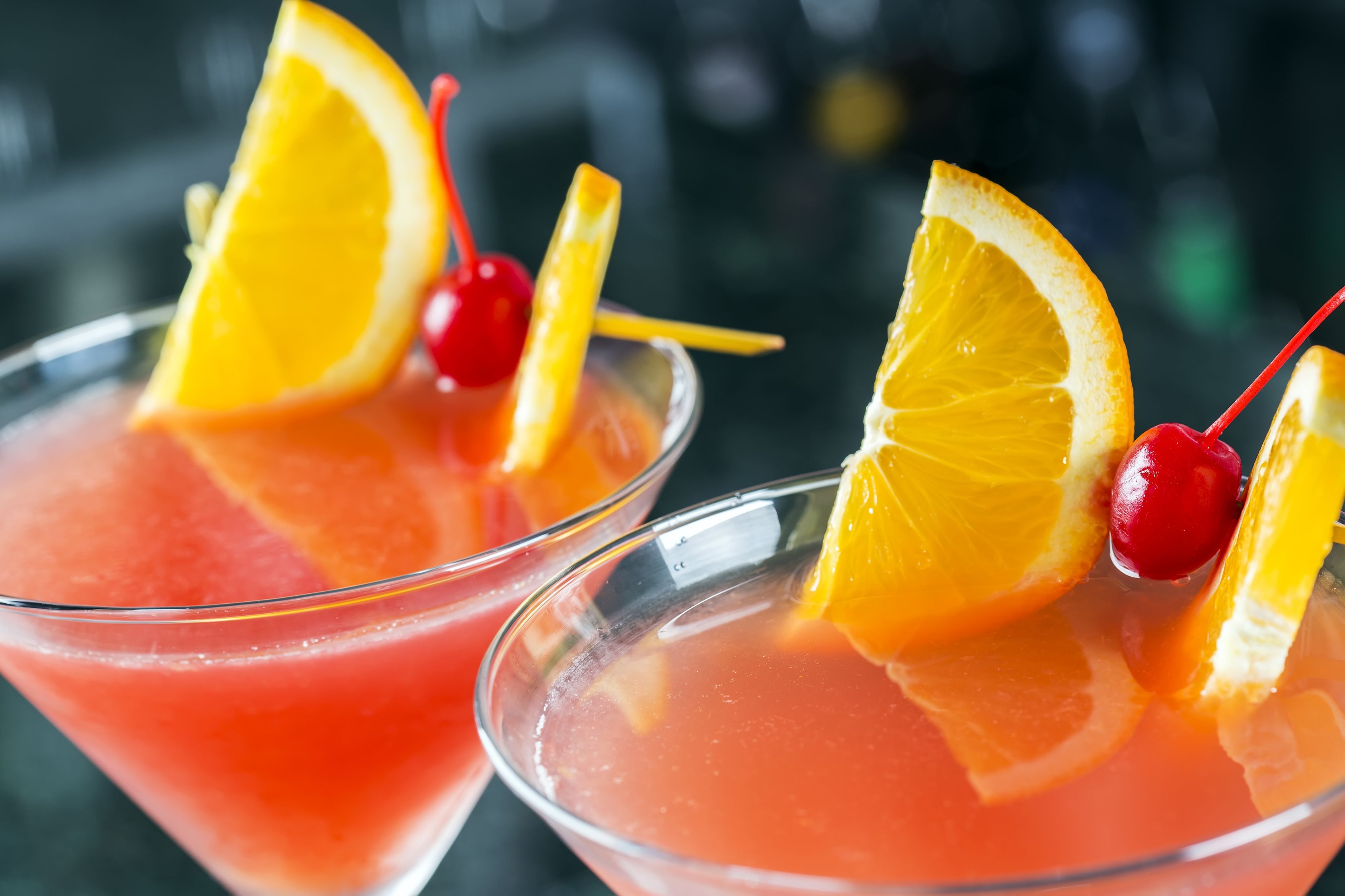 Two martini glasses filled with a pink cocktail, garnished with orange slices and cherries.