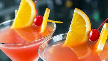 Two martini glasses filled with a pink cocktail, garnished with orange slices and cherries.