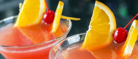 Two martini glasses filled with a pink cocktail, garnished with orange slices and cherries.