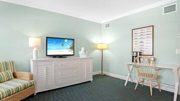 A room with a television on a white dresser, a wicker sofa, a dining table with chairs, and a wall-mounted fish chart.