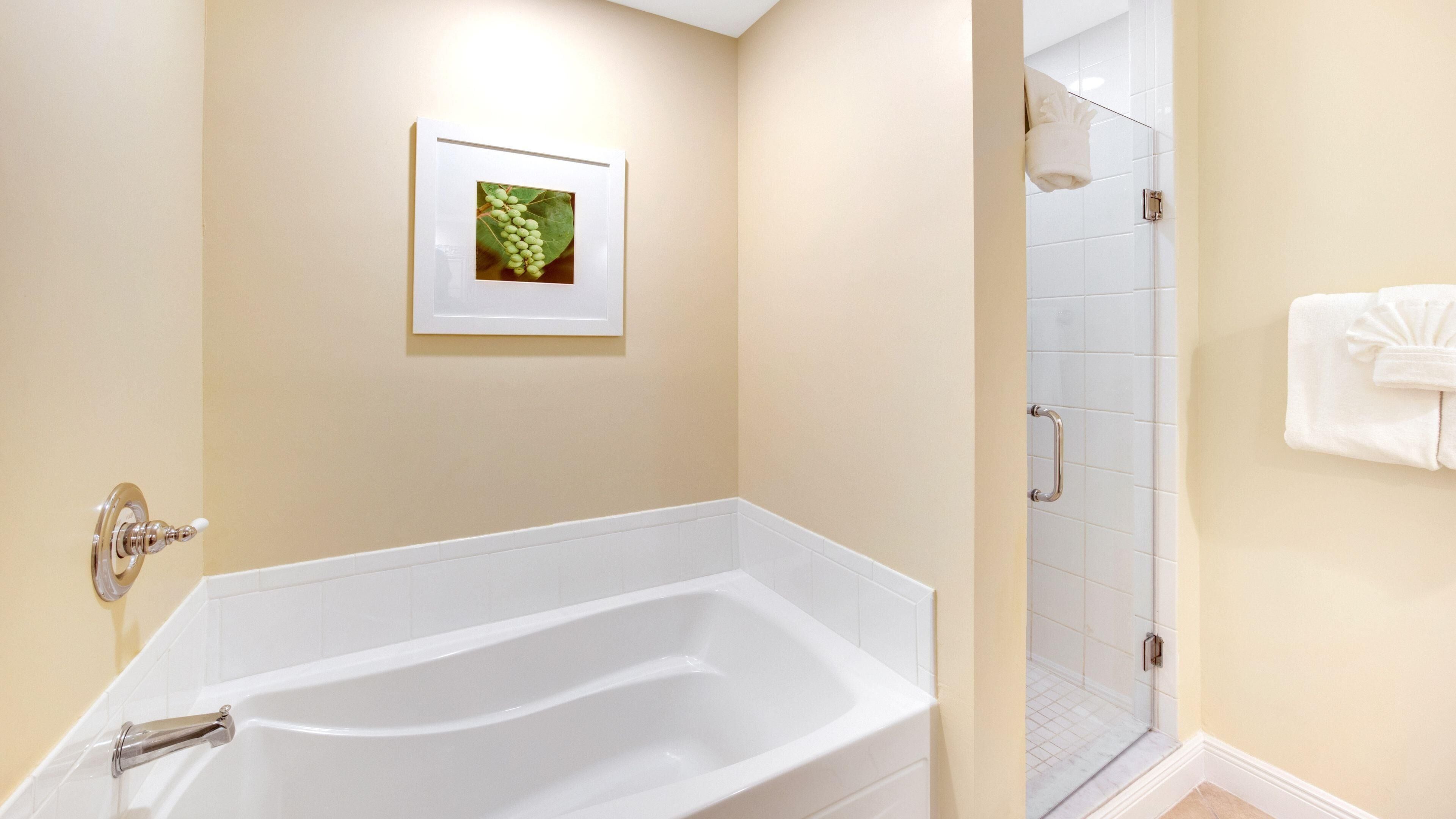 A bathroom with a white bathtub, a glass shower enclosure, and a framed picture on the wall.