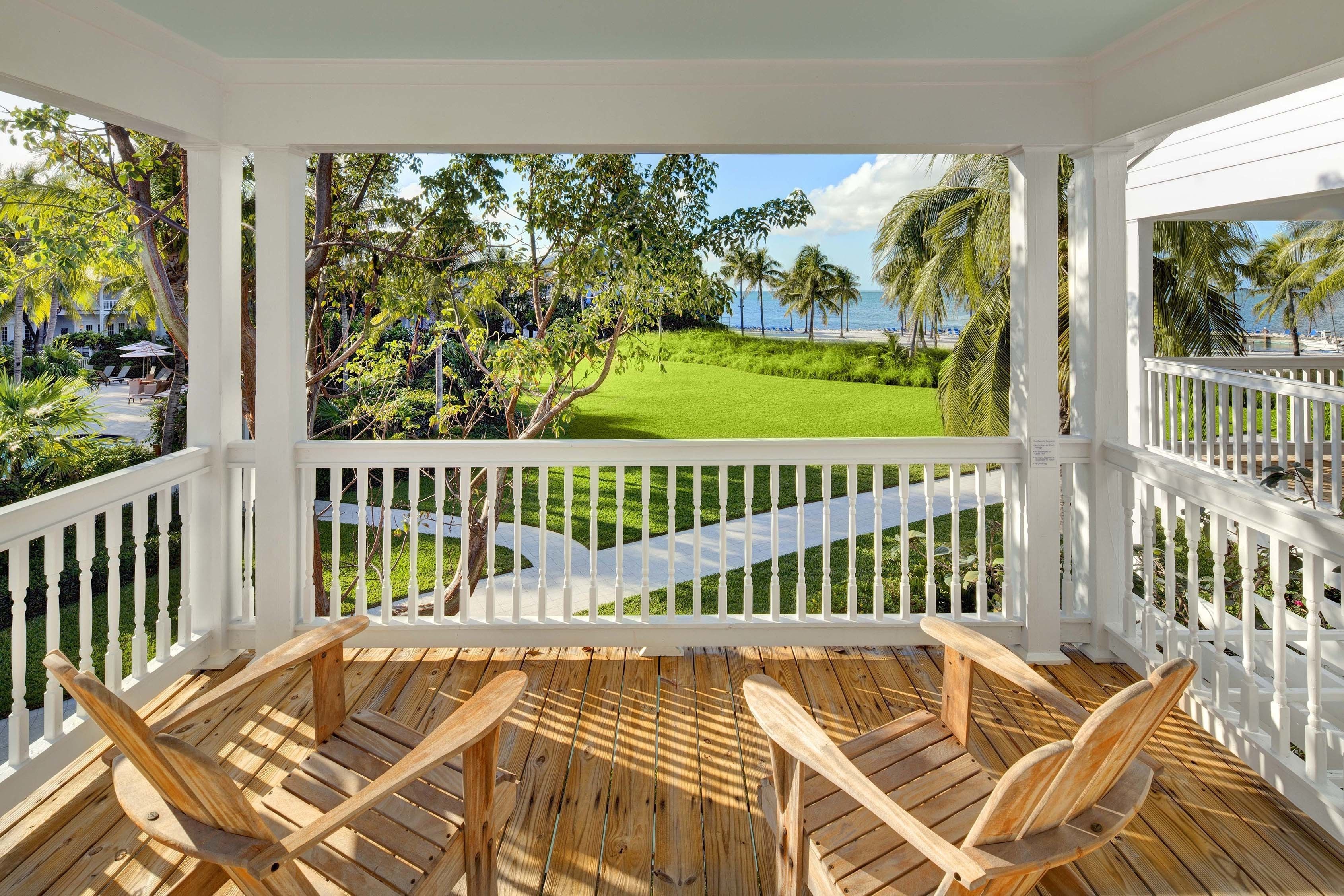 A covered outdoor area with wooden chairs and a view of a well-maintained lawn and palm trees.