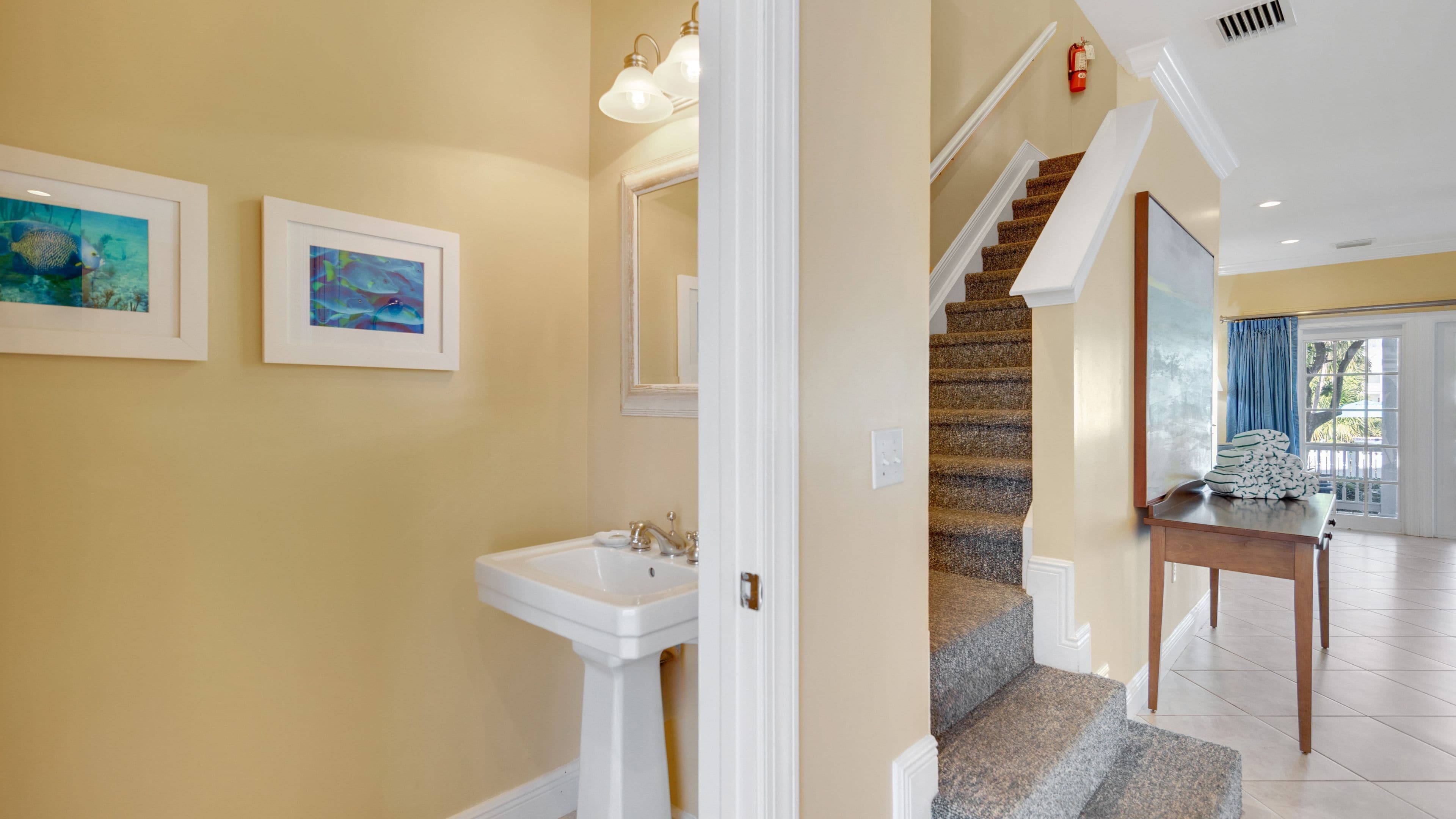 A hallway with a staircase, a sink, and two framed pictures on the wall.