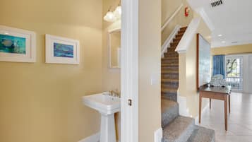 A hallway with a staircase, a sink, and two framed pictures on the wall.