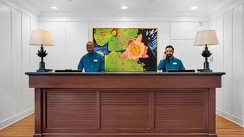 A reception desk with two staff members, a large floral painting, and two lamps.