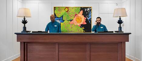 Uma receção com dois funcionários, um grande quadro floral e duas lâmpadas.