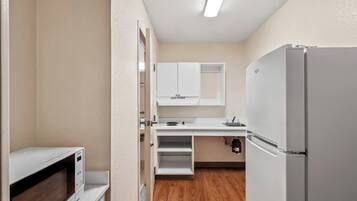 A compact kitchen with a microwave, refrigerator, and white cabinets.