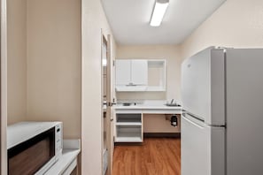 A compact kitchen with a microwave, refrigerator, and white cabinets.