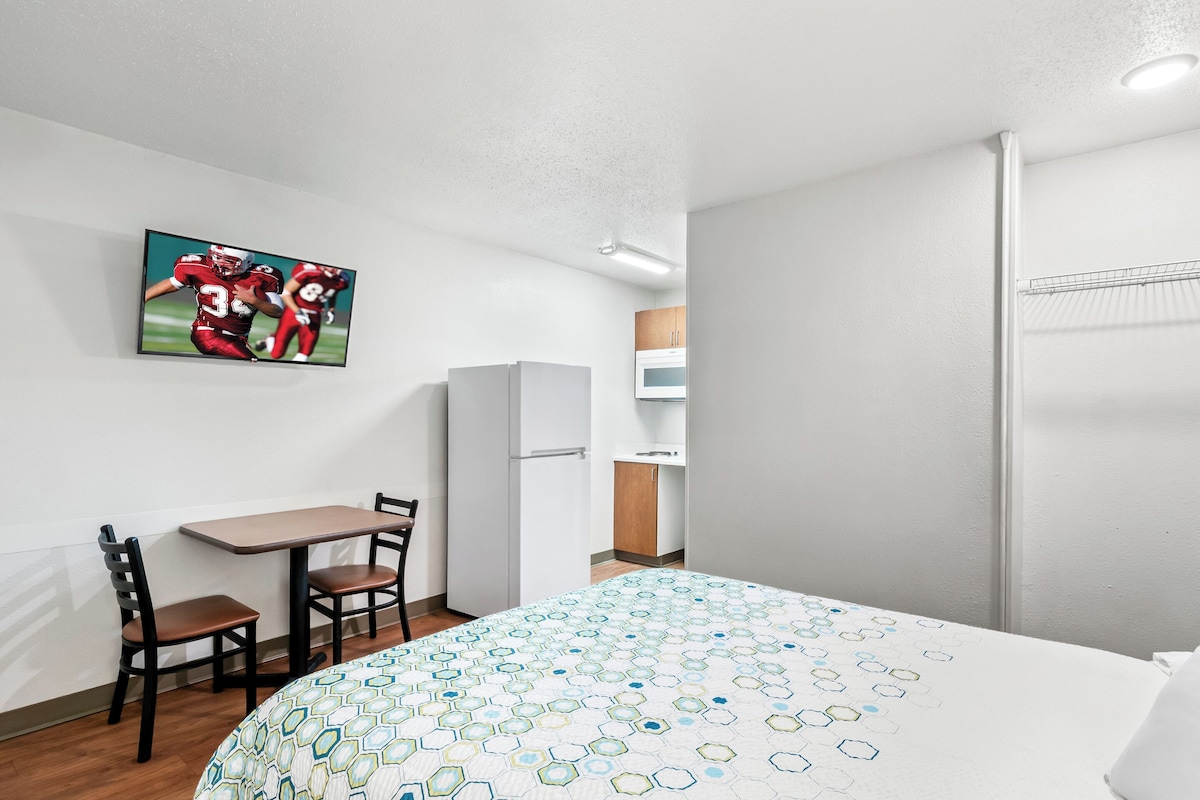 Habitación de hotel con cama, escritorio con sillas, refrigerador y microondas.