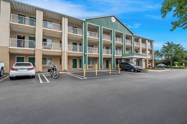 A multi-story motel with a green and beige exterior, multiple balconies, and a parking lot.