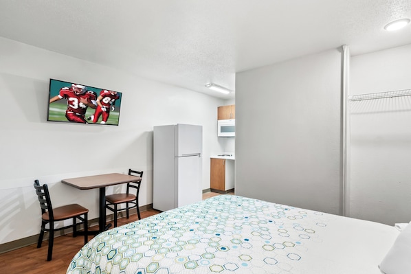 A hotel room with a bed, a desk with chairs, a refrigerator, and a microwave. - HomeTowne Studios by Red Roof Detroit - Livonia (Livonia)