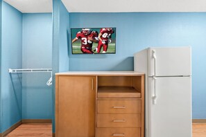 Una habitación con una pared azul, un refrigerador blanco, un mueble de madera con cajones y una fotografía enmarcada de deportes en la pared.