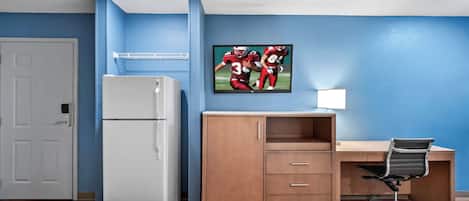 Habitación de hotel con dos camas, un escritorio, un refrigerador y un televisor en la pared.