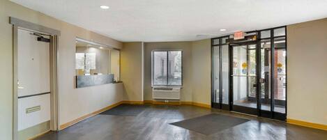A spacious lobby with a dark wooden floor, a glass door entrance, and a wall-mounted air conditioning unit.