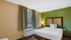 A hotel room with a bed, a window with curtains, a bedside lamp, and an air conditioning unit. - Extended Stay America Suites Philadelphia Airport Bartram Av (Philadelphia)