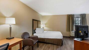 Habitación de hotel con cama, dos sillas, escritorio, lámpara, televisor y ventana con cortinas.